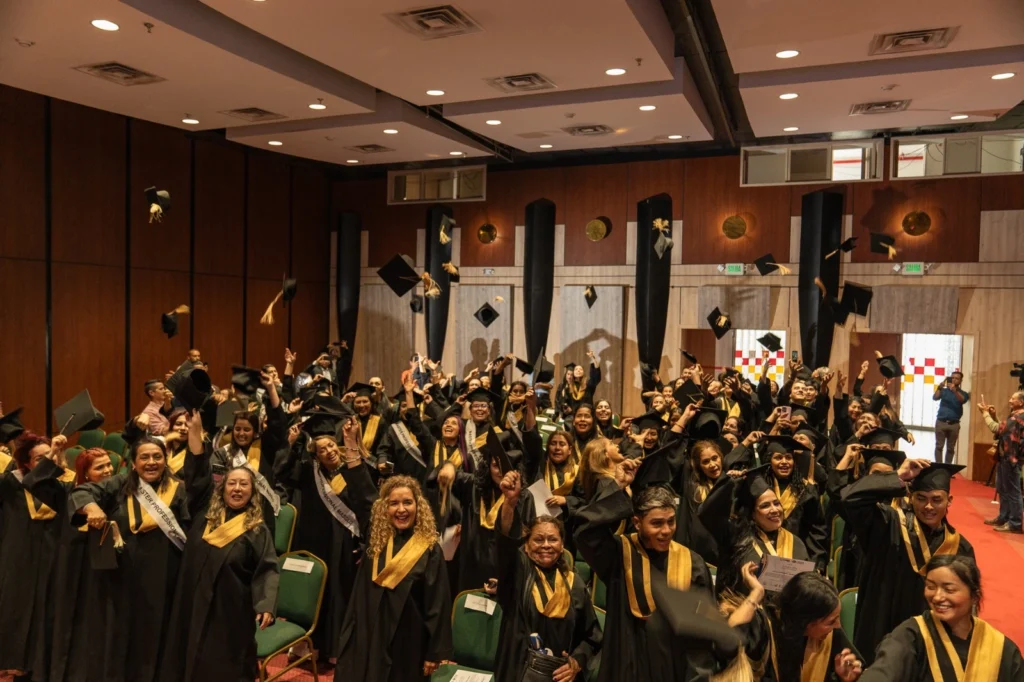 Fotografía de graduados lanzando al aire sus birretes en un auditorio.